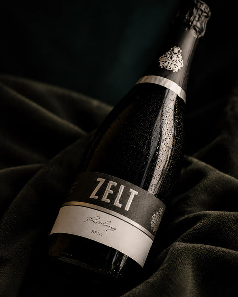 Winzersekt Riesling SEkt von Weingut Mario Zelt liegt auf einem weichen Tuch und wird von einem natürlichem Lichtkegel vom Fenster aus beleuchtet.